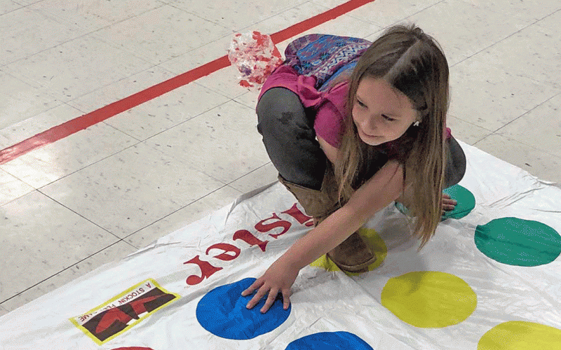 Kindergarten student, Alyssa trying to keep her balance on the Twister game board during the recent SJS K-4 event.
